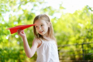 Adorable little girl holding a paper plane outdoors on sunny summer day